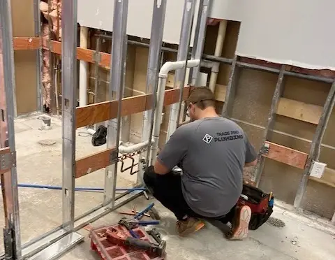 Trade Pro plumber re-running drain lines inside opened steel-stud walls during a commercial restroom remodel