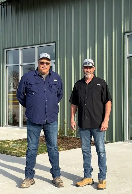 Two men in caps standing in front of a green metal building